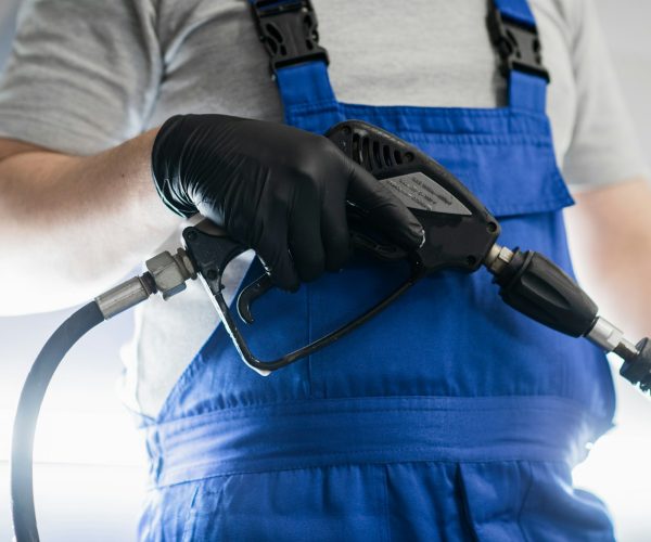 Car washing and detailing. Professional worker is washing a black car by pressure washer at a car